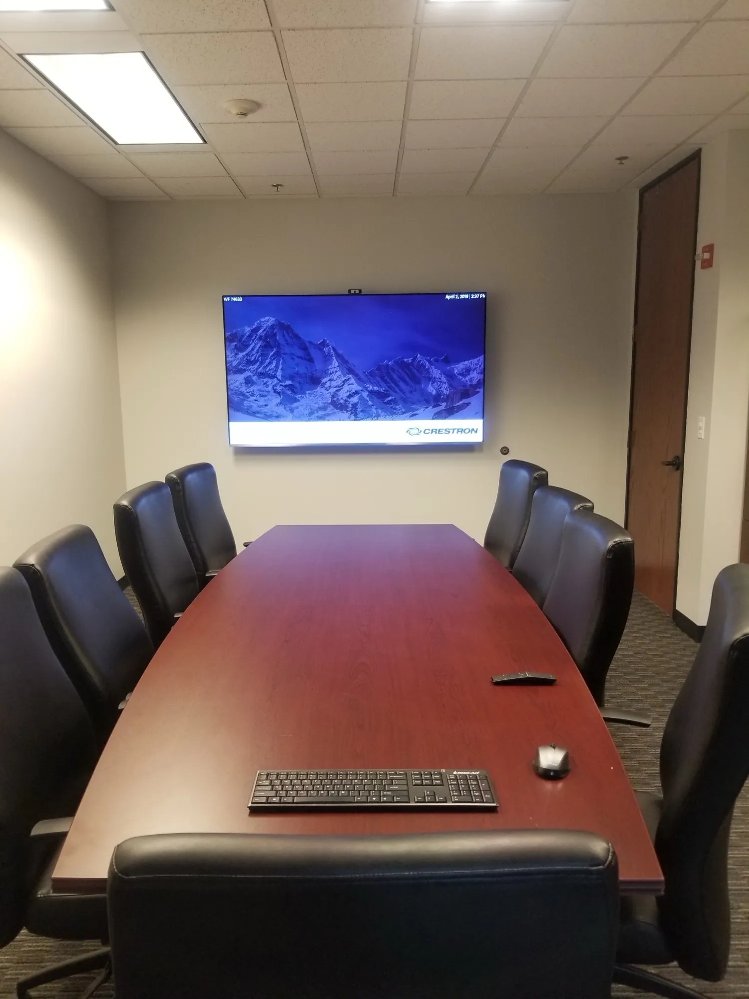 Office conference room with a wall-mounted display running Crestron, a camera above the screen, and seating for ten.