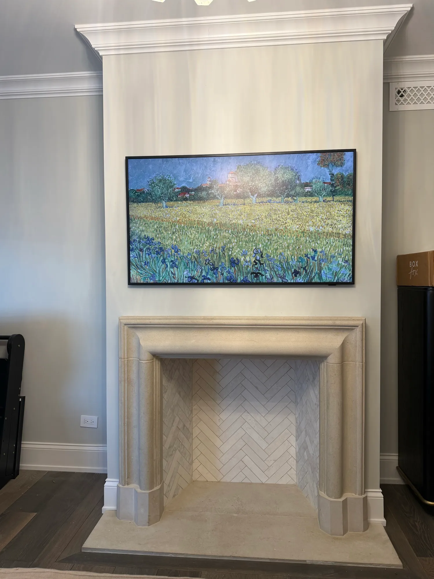 A Frame television showing a Van Gogh painting, mounted on a limestone chimney breast above a carved stone fireplace.
