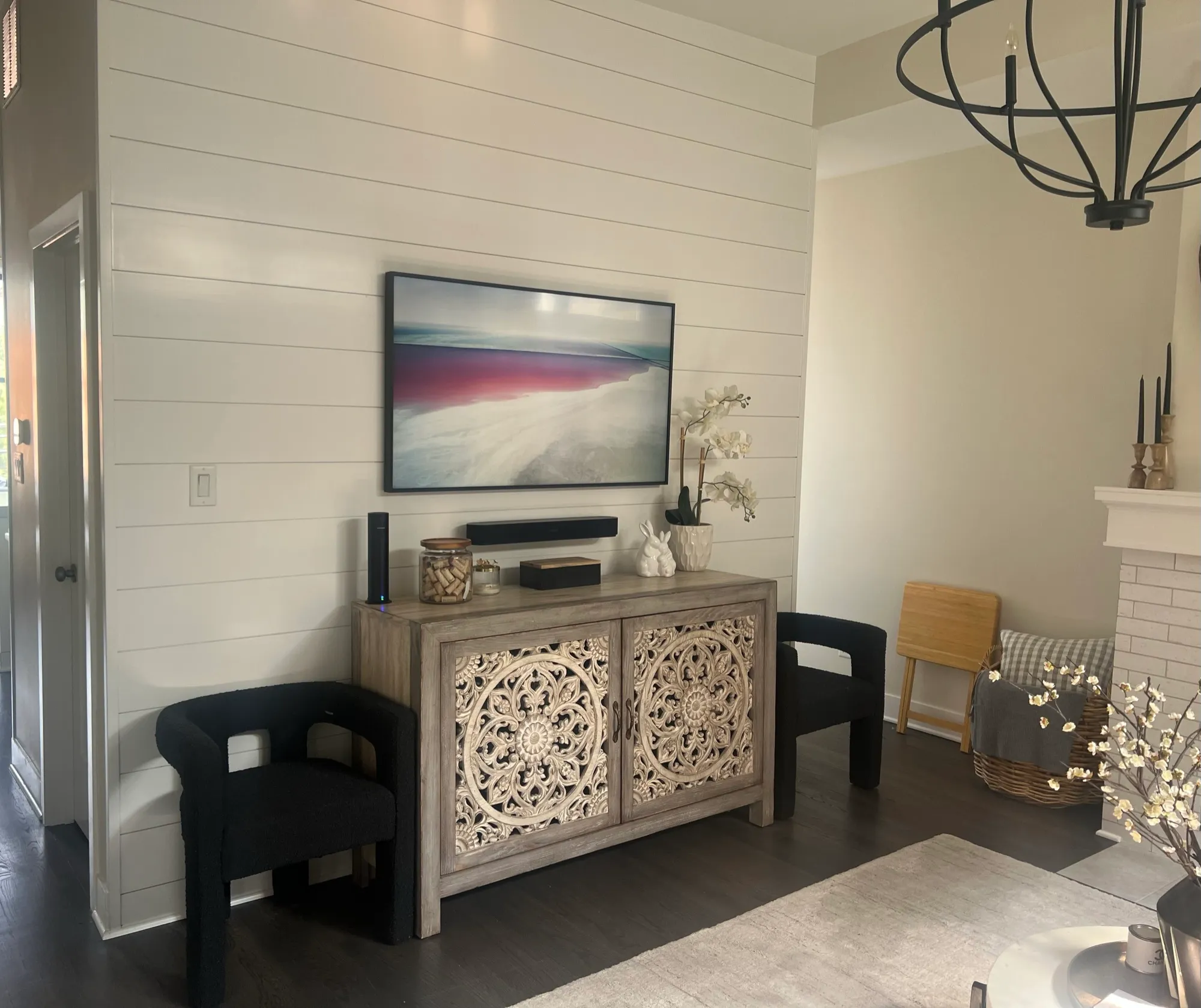 A Samsung Frame television displaying artwork on a white shiplap wall above a carved wood console.