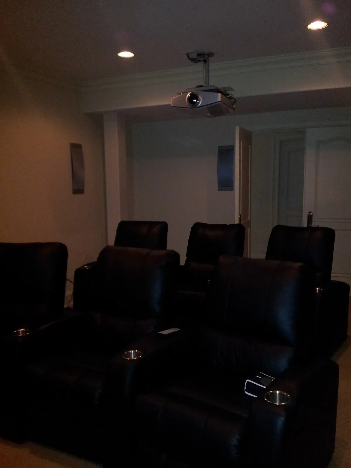 Basement home theater with two tiered rows of leather recliners and a ceiling-mounted projector.