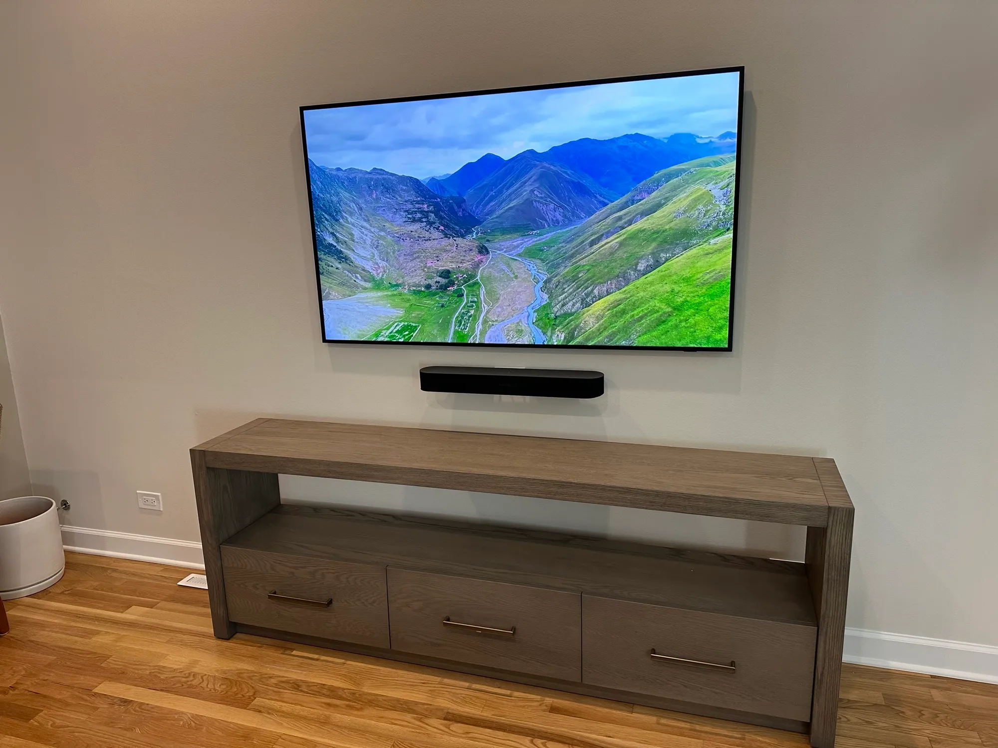 Television and soundbar wall-mounted above a low oak credenza in a bright living room.