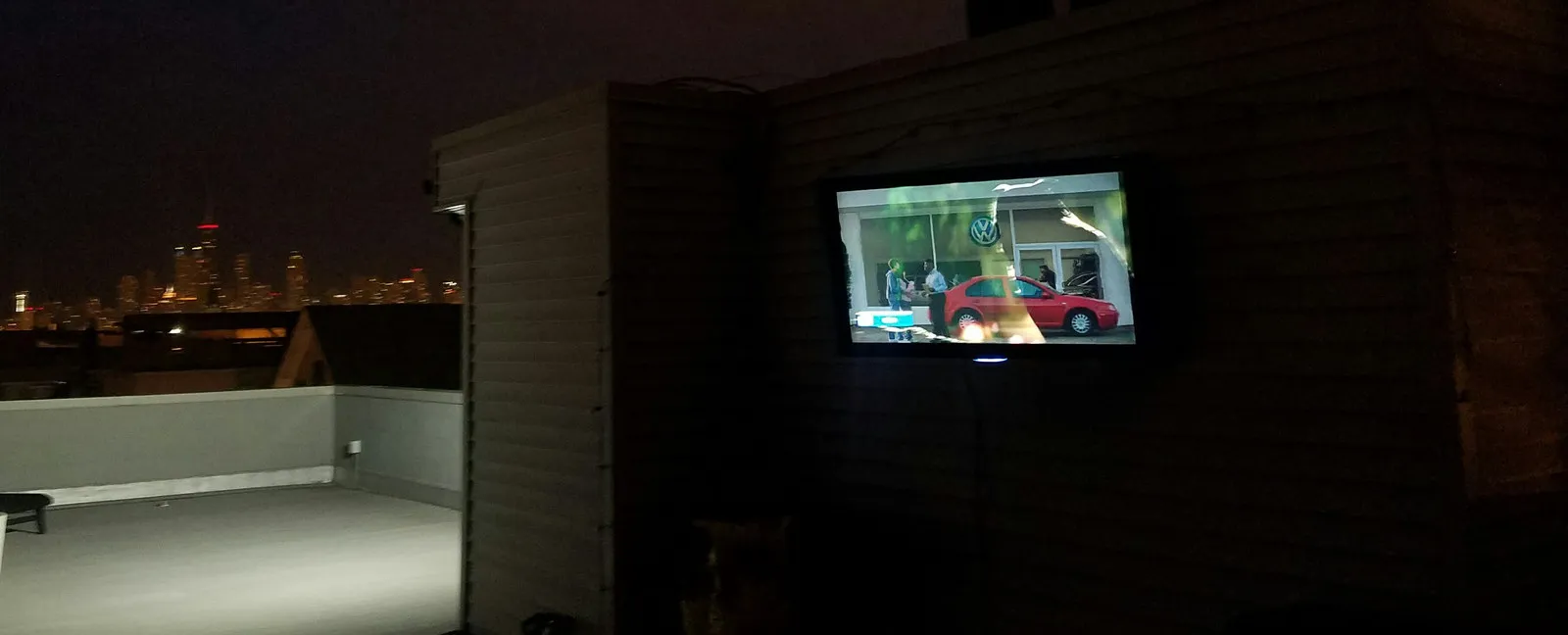 Weatherproof television mounted on a rooftop deck at night with the Chicago skyline lit in the distance.
